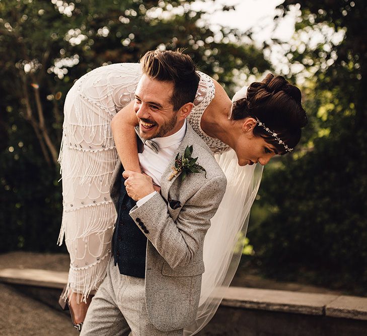 Groom with dark hair in grey suit throws bride with dark hair in updo over his shoulder