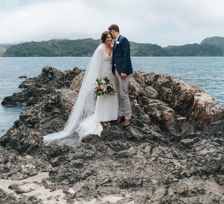 Bride in Estelle Sally Eagle Gown | Groom in Chinos & Blazer | Outdoor Coastal Wedding at Ohawini Bay in New Zealand with Natural Garden Party Reception | Miss Gen Photography