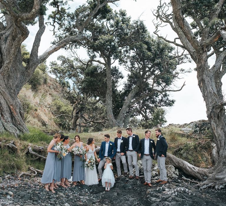 Wedding Party | Bride in Estelle Sally Eagle Gown | Bridesmaids in Powder Blue Evolution Clothing Dresses | Groomsmen in Grey Chinos & Navy Blazers | Outdoor Coastal Wedding at Ohawini Bay in New Zealand with Natural Garden Party Reception | Miss Gen Photography