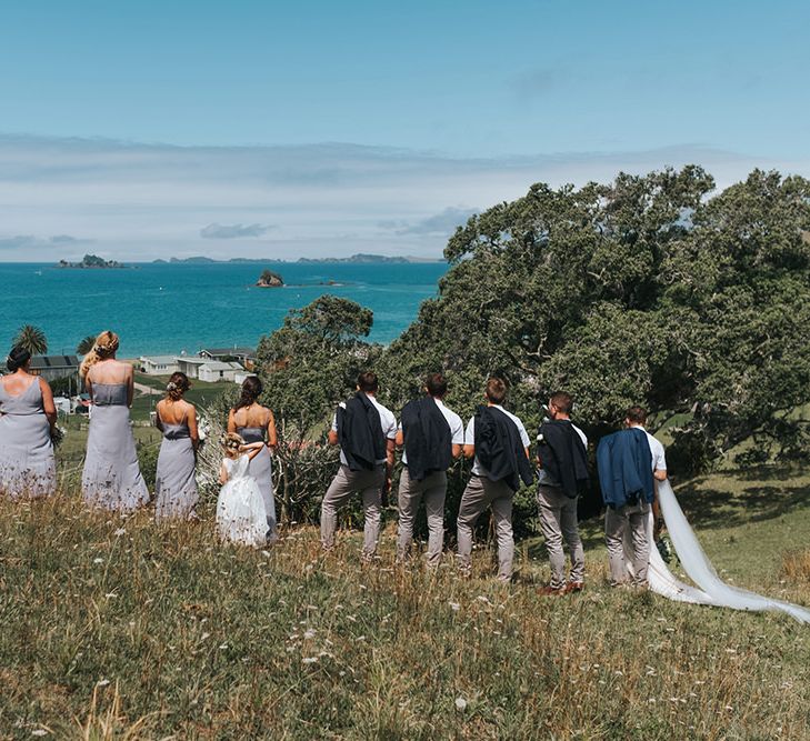 Wedding Party | Bride in Estelle Sally Eagle Gown | Bridesmaids in Powder Blue Evolution Clothing Dresses | Groomsmen in Grey Chinos & Navy Blazers | Outdoor Coastal Wedding at Ohawini Bay in New Zealand with Natural Garden Party Reception | Miss Gen Photography