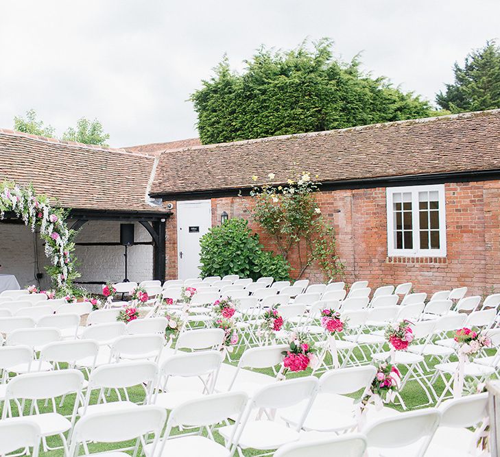 Outdoor Wedding Ceremony With White Chairs & Pink Floral Chairbacks