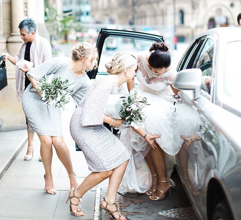 Bridesmaids help bride get into wedding car