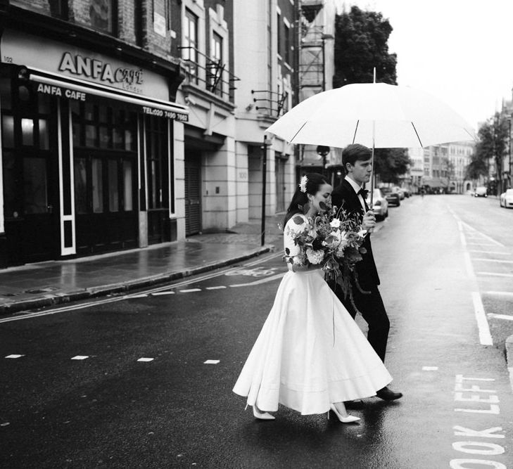 Elegant Bride in Delphine Manivet Prospere Wedding Dress & Groom in Velvet Jacket & Trousers Under an Umbrella