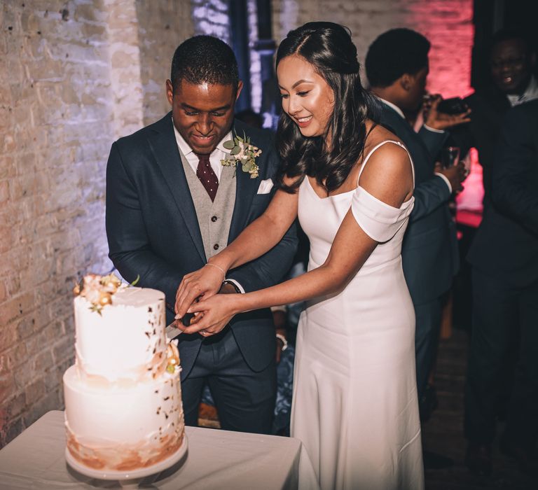 Cutting the Cake | Bride in Reformation Poppy Gown | Groom in Tailored The Bespoke Club Navy Suit | Stylish London Wedding Planned by Revelry Events | Story + Colour Photography