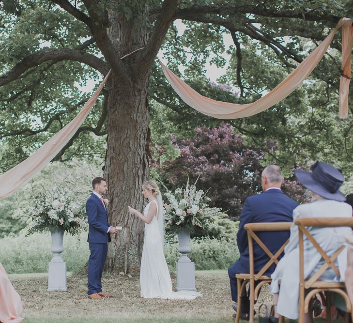 Wedding Ceremony | Bride in Justin Alexander Gown | Groom in Moss Bros Suit | Outdoor Peach Wedding at Courteenhall House in Northamptonshire Planned by Your Story Events | Ferri Photography