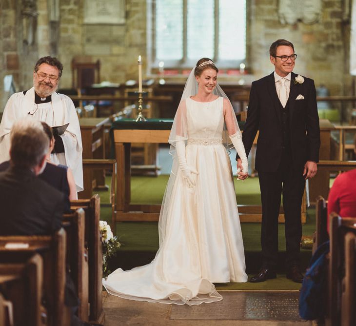 Bride in Tom Flowers Dress, Long Satin Gloves & Ivory & Co. Headdress and Groom in Moss Bros Suit at Church Wedding Ceremony