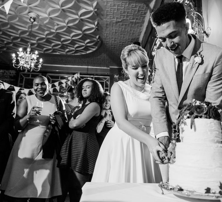 Cutting The Cake | Bride in Bespoke Tea Length Wedding Dress | Groom in Grey Jaeger Suit | 60s Inspired London Pub Wedding | The Peasant | Babb Photo