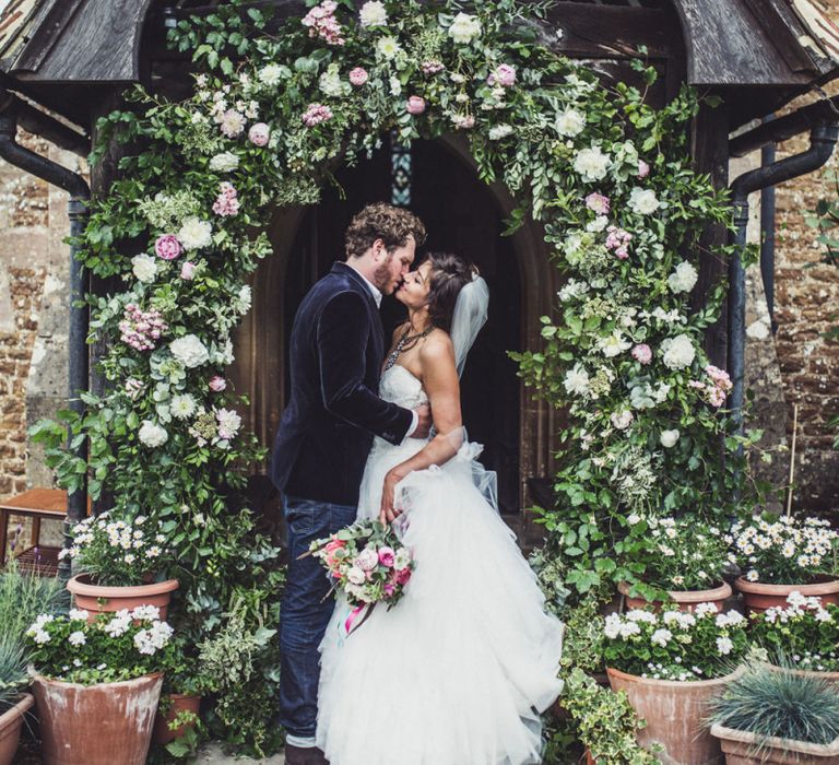 Bride and Groom Standing in Front of The Church Under a Floral Archway