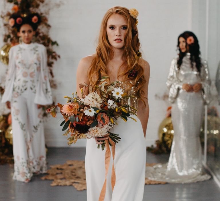 Bride in white trousers and gold corset holding an autumn bouquet