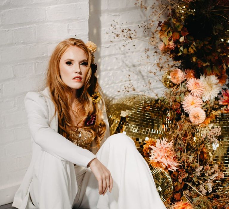 Bride in white bridal suit sitting next to gold glitter balls