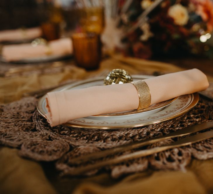 Place setting with brown mat, peach napkin and gold cutlery