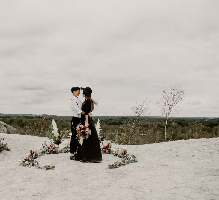 Horseshoe Pampas Grass, Eucalyptus &amp; Red Rose Floral Arrangement  | Bride in Portez Vos Idées Black Wedding Dress | Bride in Black Trousers, White Shirt &amp; Braces | Wild Same Sex Couple Wedding Inspiration Shoot | Anne Letournel Photography