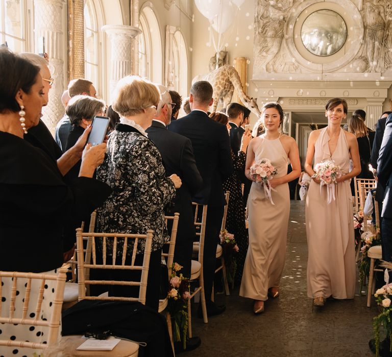 Bridesmaids in pink dresses walking down the aisle at Aynhoe Park