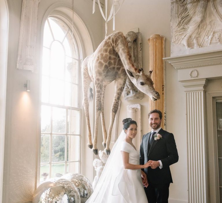 Bride and groom portrait standing in front of the infamous hanging giraffe at Aynhoe Park