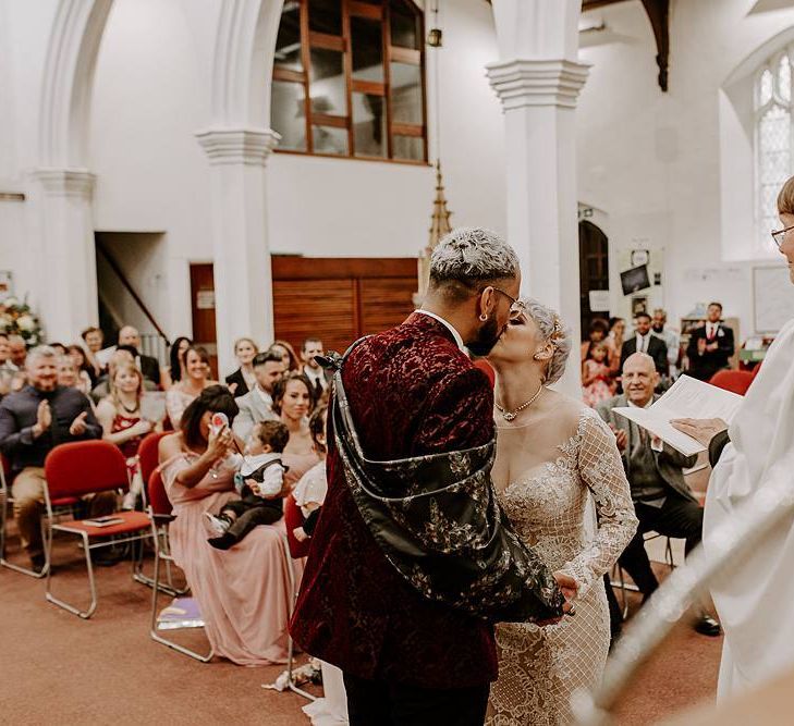 Groom in red blazer and bride in Lillian West wedding dress kissing at the altar