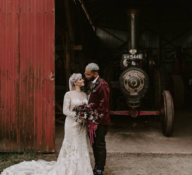 Bride in Lillian West wedding dress and groom in pink blazer next to a steam engine