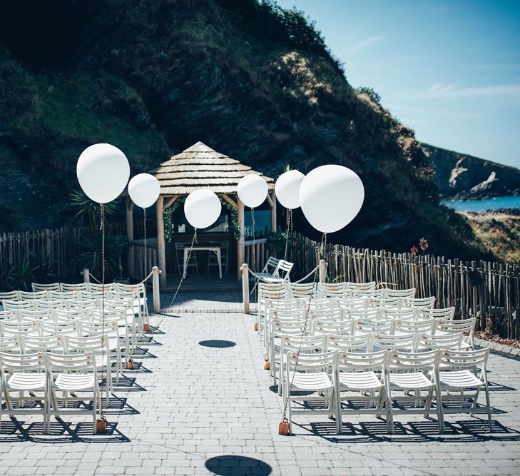 Oversized White Balloons | Gypsophila Wedding Arch | White Chairs | Wedding Ceremony Décor for Nuptials by the Sea | Gypsophila Arch and Giant Balloons for an Outdoor Coastal Wedding | Toby Lowe Photography