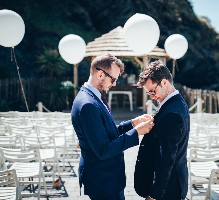 Buttonhole Being Pinned to Groom's Suit | Groom in Navy Suit | Gypsophila Arch and Giant Balloons for an Outdoor Coastal Wedding | Toby Lowe Photography