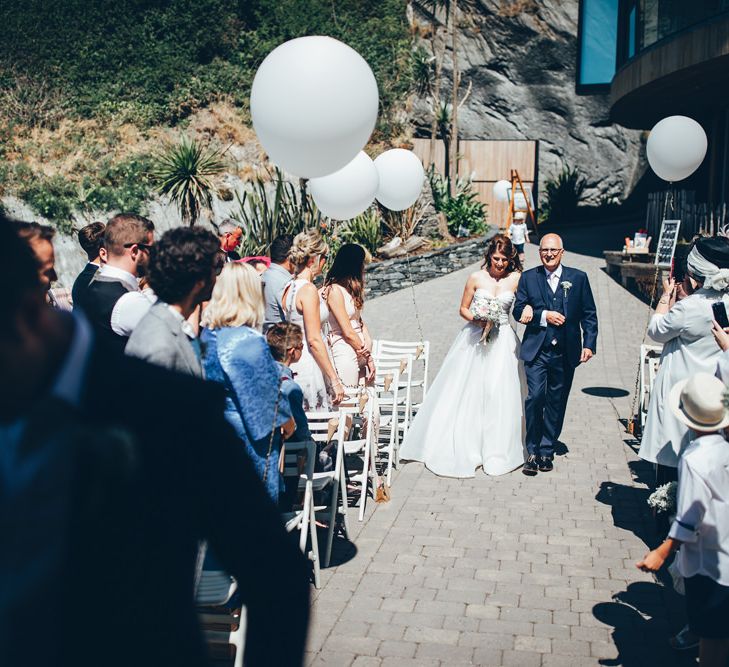 Bride in Strapless Ballgown Dress by Pronovias with Crystal Belt | Bridal Bouquet of Pink Gerberas, White Gerberas and Gypsophila Tied with Pink Trailing Ribbon | Father of the Bride in Navy Three Piece Suit with Pink Tie | Oversized White Balloons with Foliage String | Arrival of the Bride | Gypsophila Arch and Giant Balloons for an Outdoor Coastal Wedding | Toby Lowe Photography