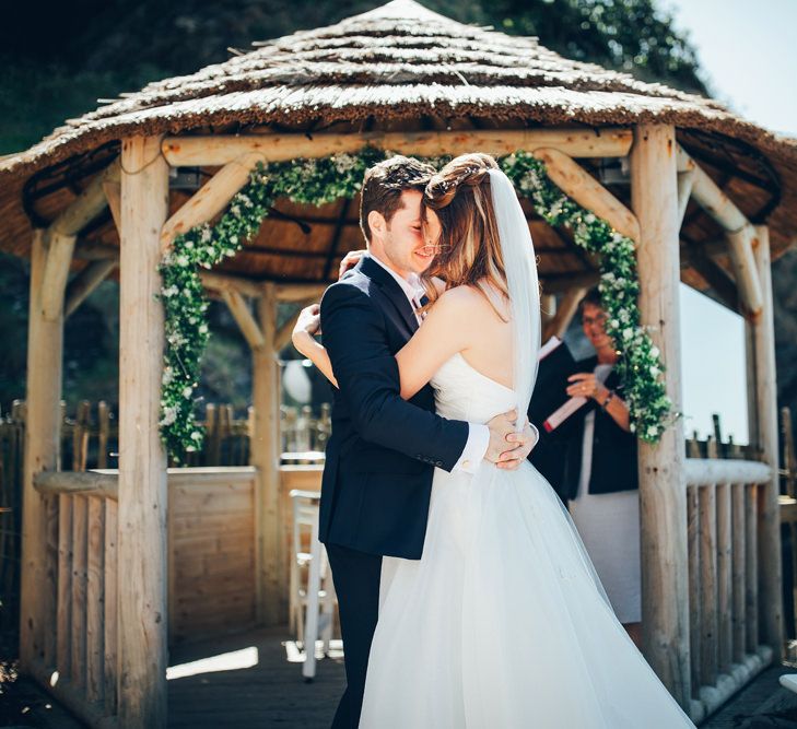 Bride in Strapless Ballgown Dress by Pronovias with Crystal Belt | Fingertip Veil | Groom in Navy Suit with Gypsophila Buttonhole | Gypsophila Wedding Arch | Wedding Ceremony | Gypsophila Arch and Giant Balloons for an Outdoor Coastal Wedding | Toby Lowe Photography