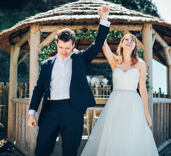 Bride in Strapless Ballgown Dress by Pronovias with Crystal Belt | Groom in Navy Suit with Gypsophila Buttonhole | Gypsophila Wedding Arch | Wedding Ceremony | Gypsophila Arch and Giant Balloons for an Outdoor Coastal Wedding | Toby Lowe Photography