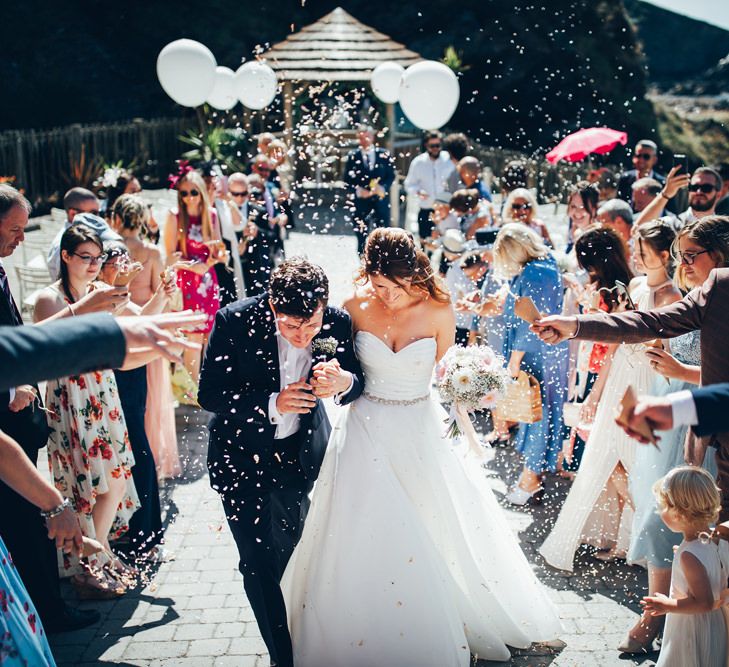 Bride in Strapless Ballgown Dress by Pronovias with Crystal Belt | Bridal Bouquet of Pink Gerberas, White Gerberas and Gypsophila Tied with Pink Trailing Ribbon | Groom in Navy Suit with Gypsophila Buttonhole | Confetti Throw | Oversized White Balloons with Foliage String | Gypsophila Arch and Giant Balloons for an Outdoor Coastal Wedding | Toby Lowe Photography