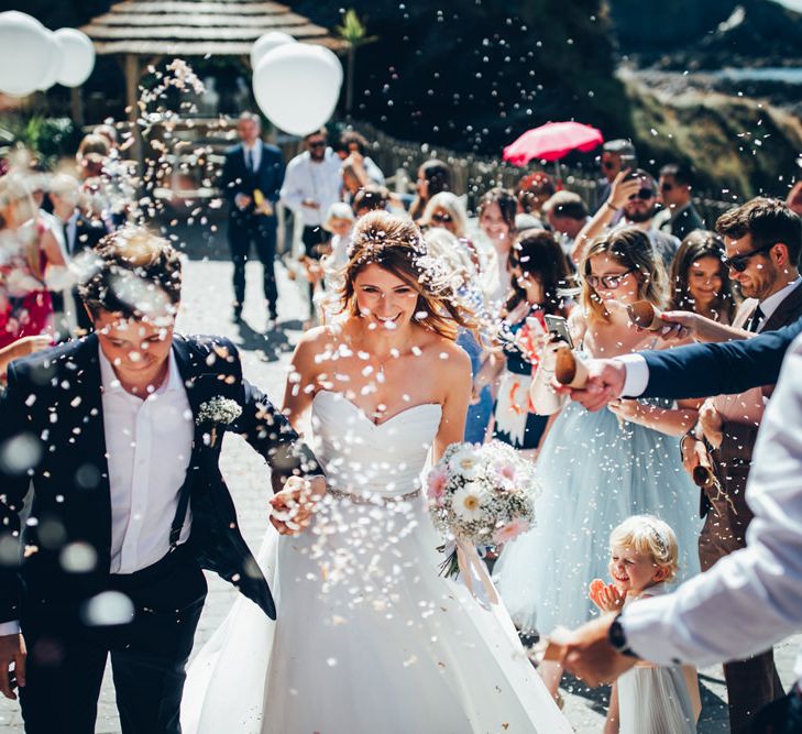 Bride in Strapless Ballgown Dress by Pronovias with Crystal Belt | Bridal Bouquet of Pink Gerberas, White Gerberas and Gypsophila Tied with Pink Trailing Ribbon | Groom in Navy Suit with Gypsophila Buttonhole | Confetti Throw | Oversized White Balloons with Foliage String | Gypsophila Arch and Giant Balloons for an Outdoor Coastal Wedding | Toby Lowe Photography