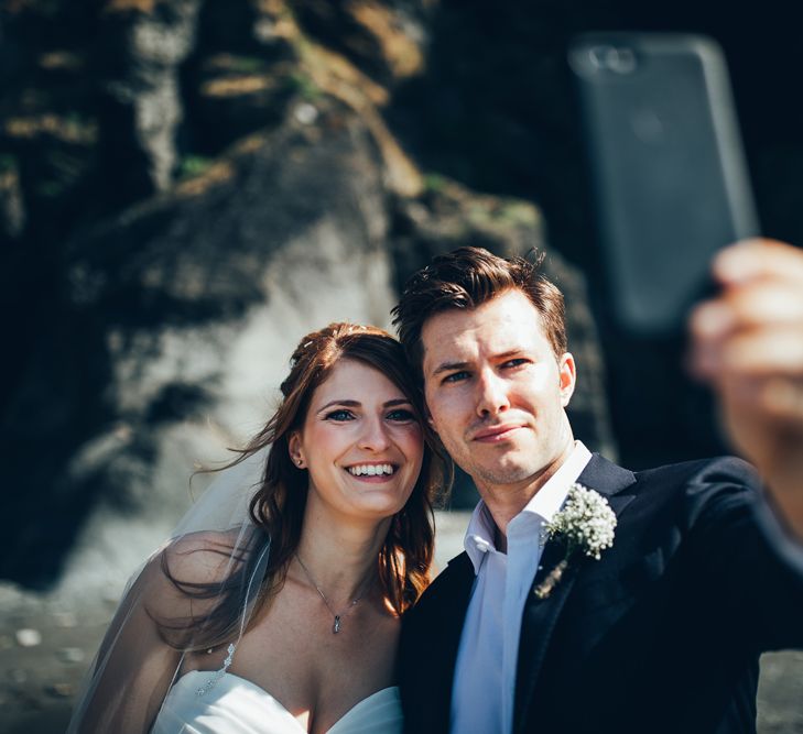 Bride in Strapless Ballgown Dress by Pronovias with Crystal Belt | Groom in Navy Suit with Gypsophila Buttonhole | Wedding Selfie | Gypsophila Arch and Giant Balloons for an Outdoor Coastal Wedding | Toby Lowe Photography