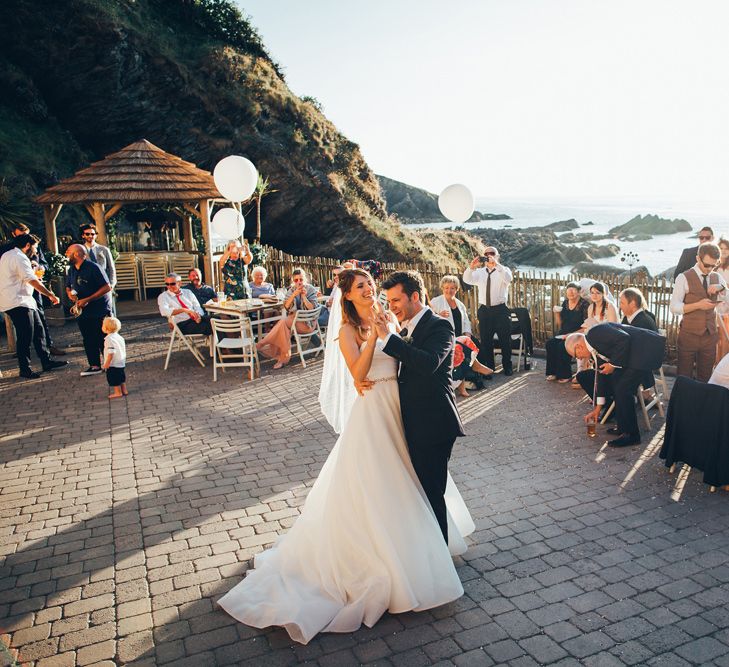 Bride in Strapless Ballgown Dress by Pronovias with Crystal Belt | Fingertip Veil | Groom in Navy Suit with Gypsophila Buttonhole | Oversized White Balloons with Foliage String | First Dance | Gypsophila Arch and Giant Balloons for an Outdoor Coastal Wedding | Toby Lowe Photography