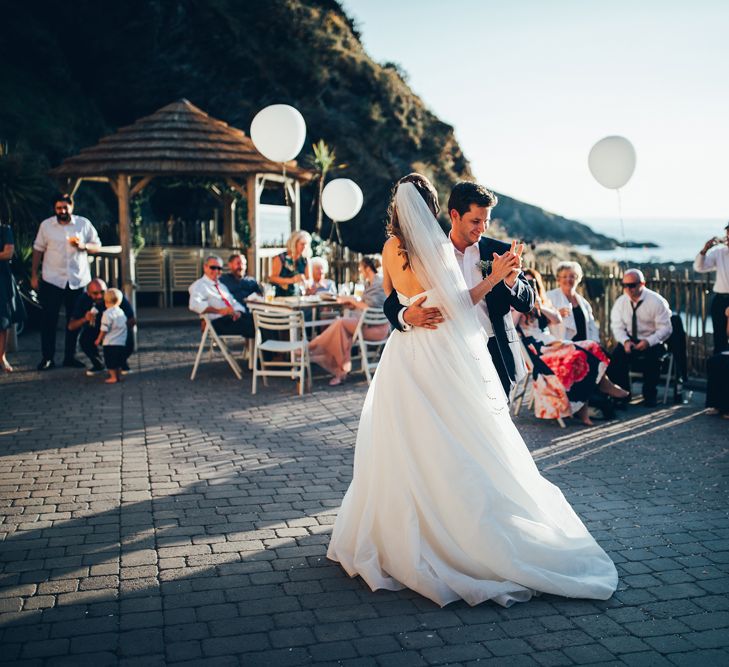 Bride in Strapless Ballgown Dress by Pronovias with Crystal Belt | Fingertip Veil | Groom in Navy Suit with Gypsophila Buttonhole | Oversized White Balloons with Foliage String | First Dance | Gypsophila Arch and Giant Balloons for an Outdoor Coastal Wedding | Toby Lowe Photography