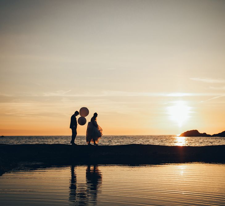 Bride in Strapless Ballgown Dress by Pronovias with Crystal Belt | Groom in Navy Suit with Gypsophila Buttonhole | Oversized White Balloons | Golden Hour Photos | Gypsophila Arch and Giant Balloons for an Outdoor Coastal Wedding | Toby Lowe Photography