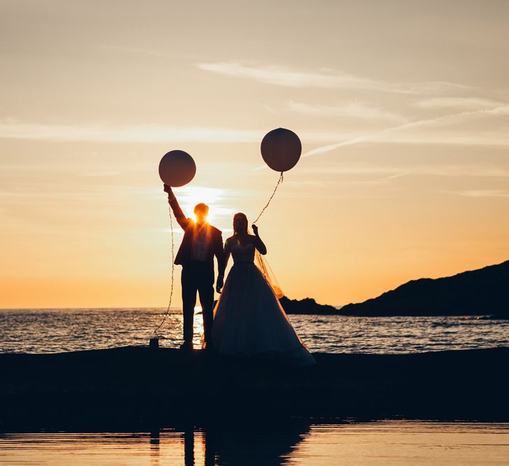 Bride in Strapless Ballgown Dress by Pronovias with Crystal Belt | Fingertip Veil | Groom in Navy Suit with Gypsophila Buttonhole |  Oversized White Balloons | Golden Hour Photos | Gypsophila Arch and Giant Balloons for an Outdoor Coastal Wedding | Toby Lowe Photography