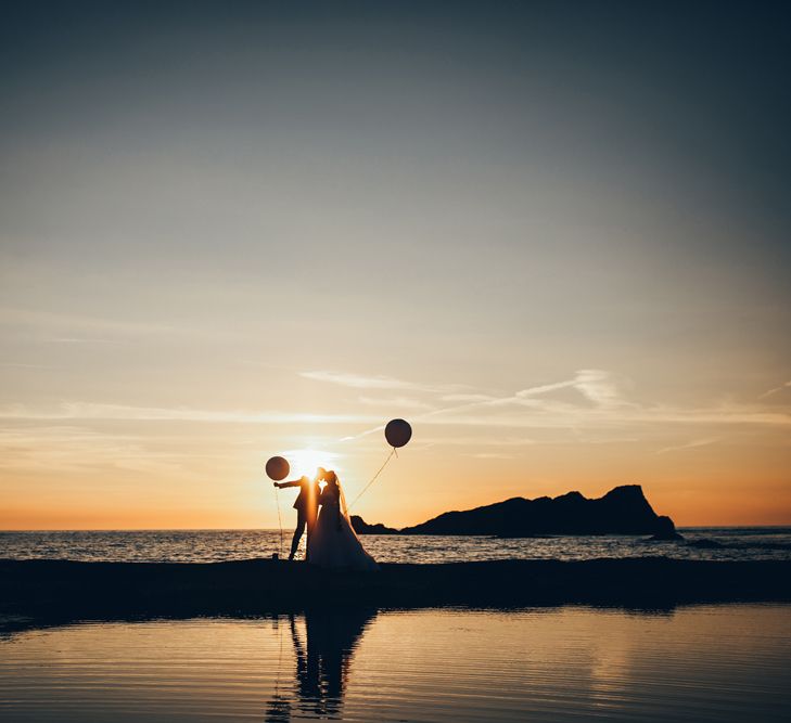 Bride in Strapless Ballgown Dress by Pronovias with Crystal Belt | Fingertip Veil | Groom in Navy Suit with Gypsophila Buttonhole |  Oversized White Balloons | Golden Hour Photos | Gypsophila Arch and Giant Balloons for an Outdoor Coastal Wedding | Toby Lowe Photography