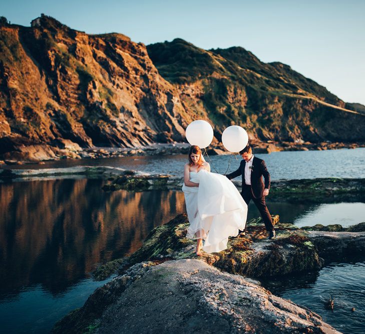 Bride in Strapless Ballgown Dress by Pronovias with Crystal Belt | Fingertip Veil | Groom in Navy Suit with Gypsophila Buttonhole |  Oversized White Balloons | Gypsophila Arch and Giant Balloons for an Outdoor Coastal Wedding | Toby Lowe Photography