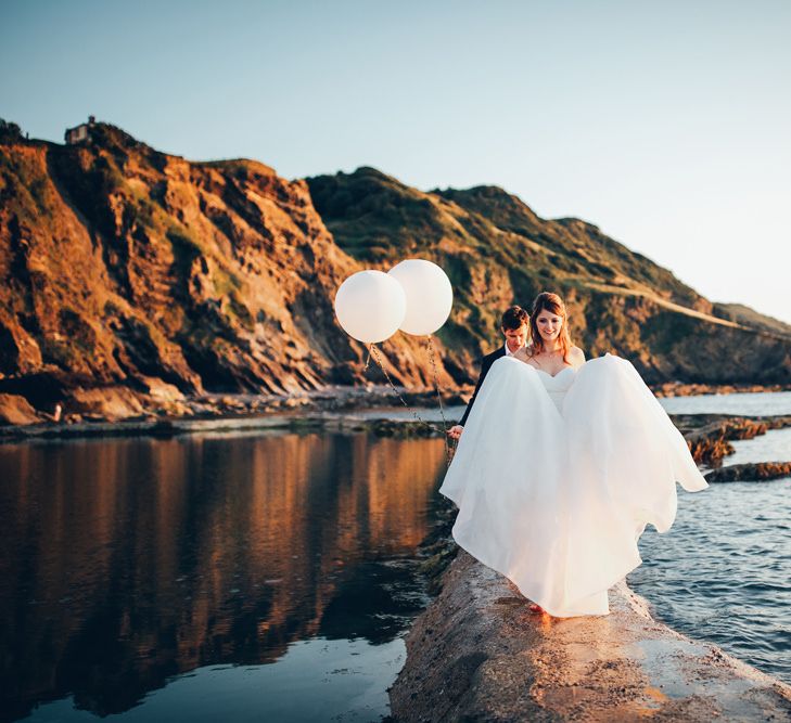 Bride in Strapless Ballgown Dress by Pronovias with Crystal Belt | Groom in Navy Suit with Gypsophila Buttonhole |  Oversized White Balloons | Gypsophila Arch and Giant Balloons for an Outdoor Coastal Wedding | Toby Lowe Photography