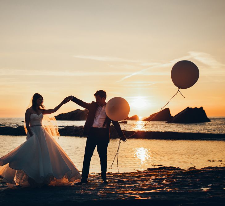 Bride in Strapless Ballgown Dress by Pronovias with Crystal Belt | Fingertip Veil | Groom in Navy Suit with Gypsophila Buttonhole |  Oversized White Balloons | Golden Hour Photos | Gypsophila Arch and Giant Balloons for an Outdoor Coastal Wedding | Toby Lowe Photography