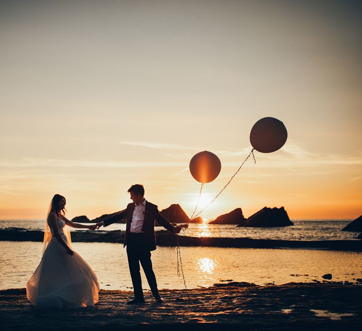 Bride in Strapless Ballgown Dress by Pronovias with Crystal Belt | Fingertip Veil | Groom in Navy Suit with Gypsophila Buttonhole |  Oversized White Balloons | Golden Hour Photos | Gypsophila Arch and Giant Balloons for an Outdoor Coastal Wedding | Toby Lowe Photography