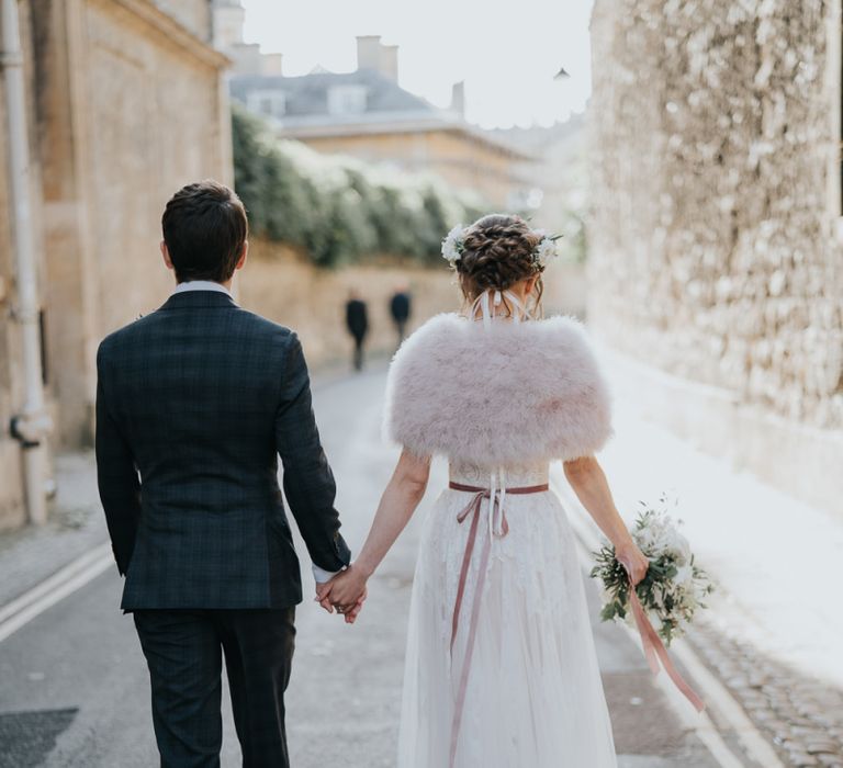 Bride and groom take a walk with their guests at an  intimate celebration with a bridal shrug and a beautiful white floral bouquet