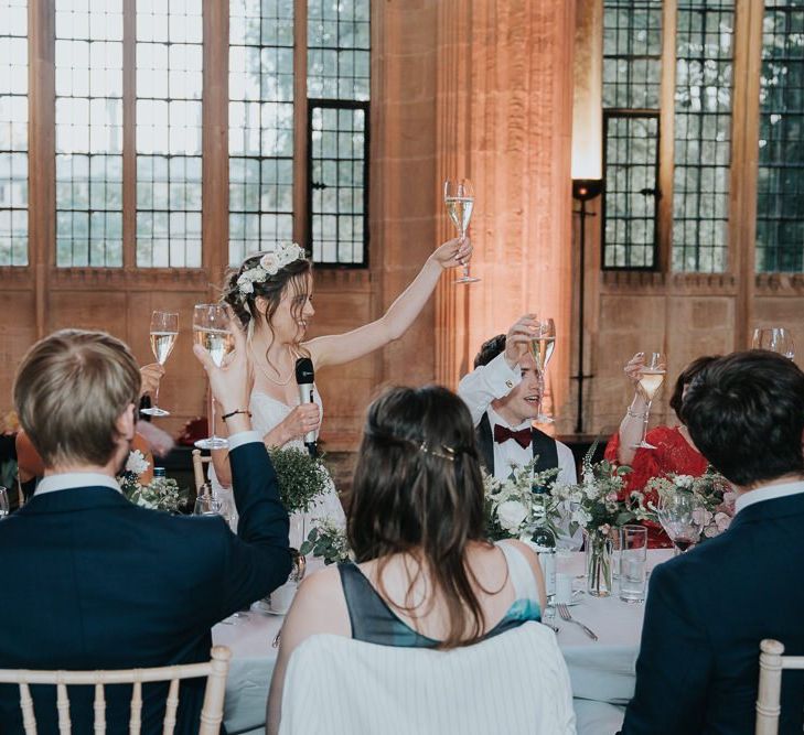 Bride raises her hand for a toast at intimate Oxford wedding reception wearing a floral head crown