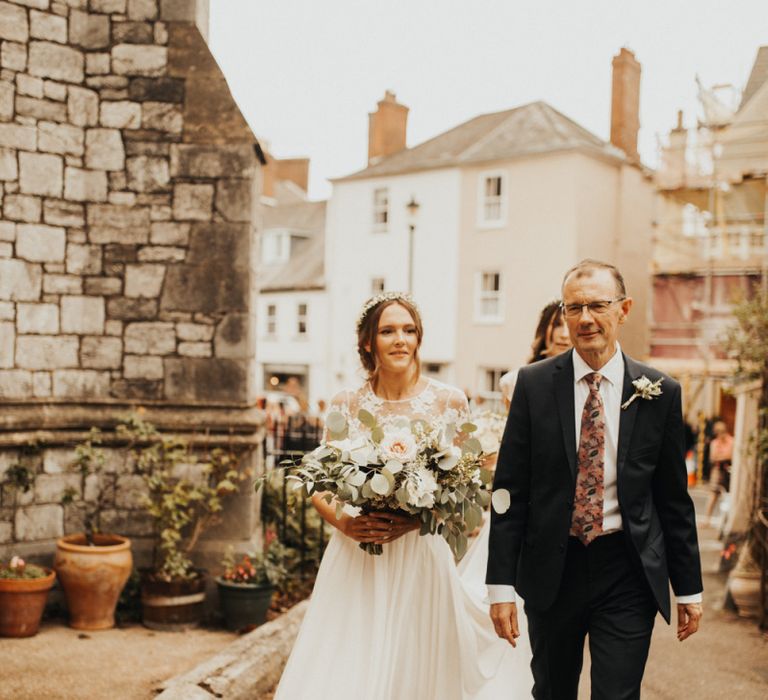 Bride arrives at church with father carrying large bouquet