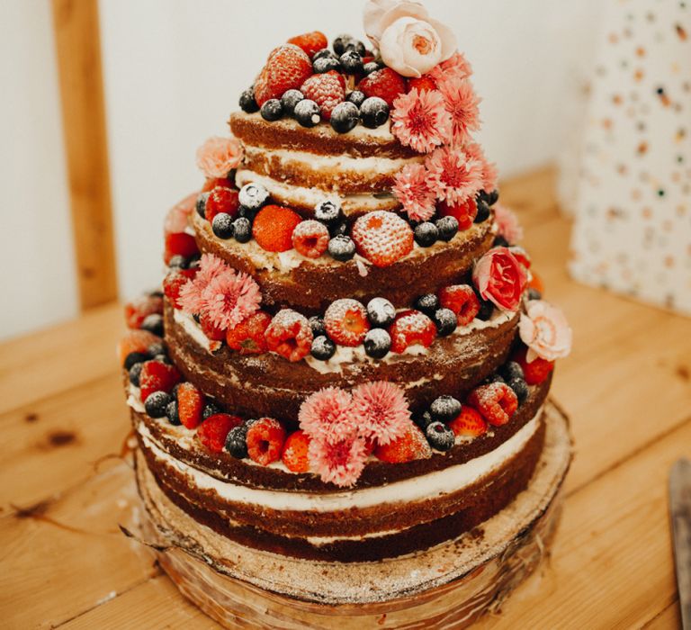 Naked wedding cake adorned in berries with foliage table runner decor