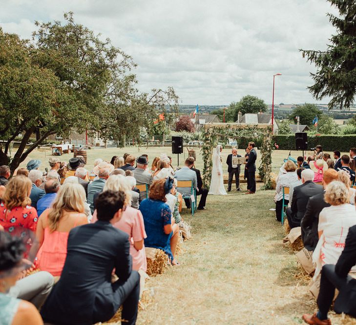 Wedding Ceremony | Bride in Laced Catherine Deane Wedding Dress with Long Sleeves | Groom in Blue Thomas Farthing Suit with Ochre Tie | Guests on Hay Bales | Rustic French Destination Wedding with Homegrown Flowers  | Emily &amp; Steve Photography