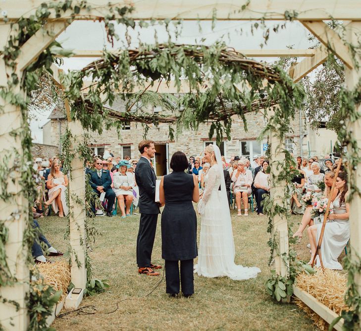 Wedding Ceremony | Foliage Arch | Bride in Laced Catherine Deane Wedding Dress with Long Sleeves | Groom in Blue Thomas Farthing Suit with Ochre Tie | Rustic French Destination Wedding with Homegrown Flowers  | Emily &amp; Steve Photography