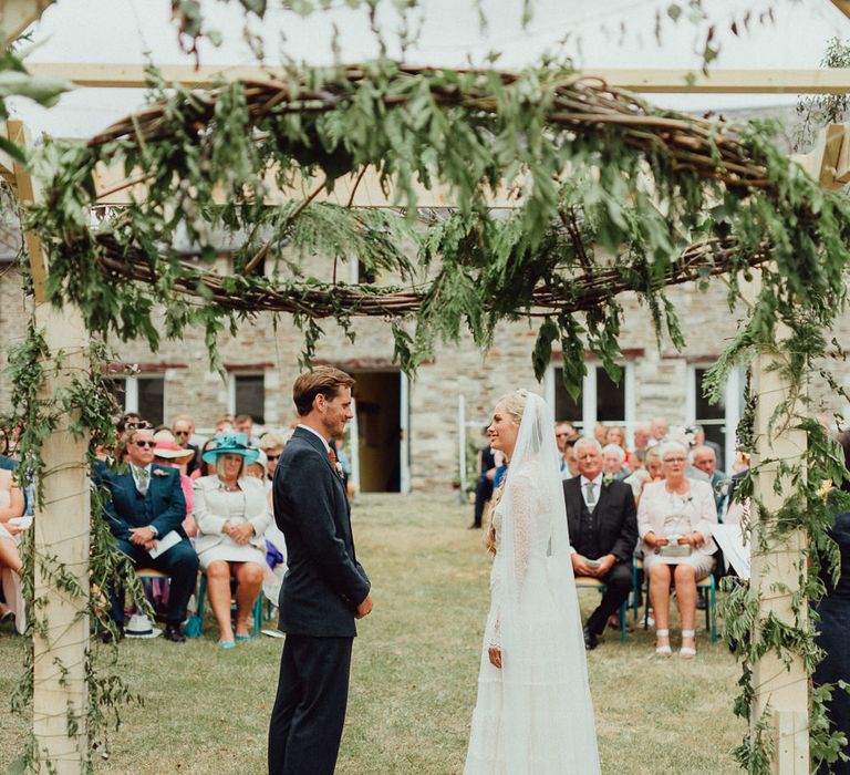 Wedding Ceremony | Foliage Arch | Bride in Laced Catherine Deane Wedding Dress with Long Sleeves | Groom in Blue Thomas Farthing Suit with Ochre Tie | Rustic French Destination Wedding with Homegrown Flowers  | Emily &amp; Steve Photography