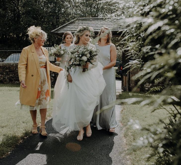 Bride wearing floral crown and white floral bouquet with her bridesmaids in silver Ghost dresses