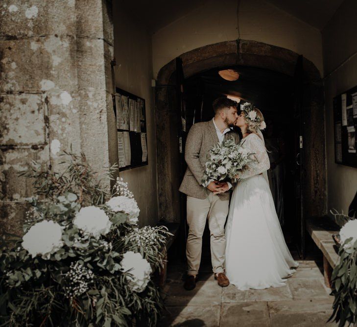 Bride and groom kiss at the church entrance with white floral decor