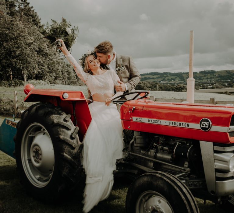 Bride and groom pose on a red tractor at relaxed country wedding