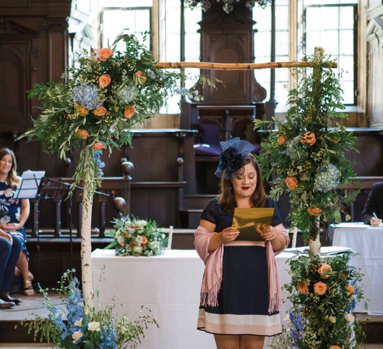 Friend Performing Wedding Reading in Front of Floral Arch