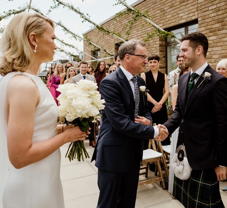 Bride clutching white rose bouquet with groom wearing traditional Scottish kilt