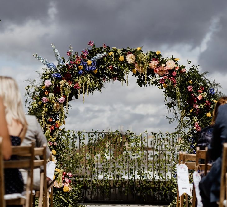 Bright multi-coloured floral moon gate at outdoor wedding with bridal jumpsuit